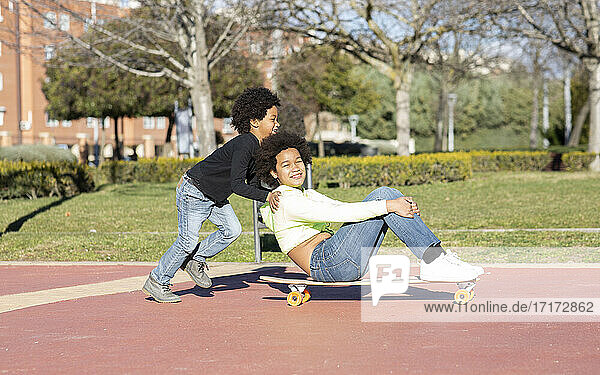 Junge schiebt seine auf einem Skateboard sitzende Schwester beim Spielen im Park