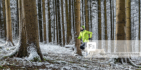 Junger männlicher Sportler läuft mit Labrador im Winter im Wald