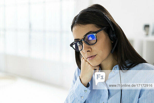 Geschäftsfrau mit Mikrofon-Headset und Brille starrt beim Sitzen im Büro