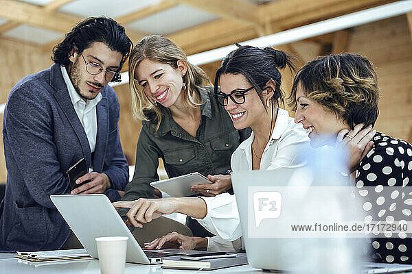 Smiling professionals discussing over laptop at office