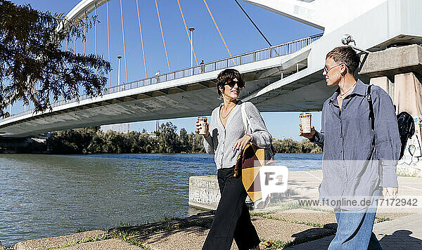 Junge Frauen mit Kaffeetasse auf dem Fußweg am Fluss