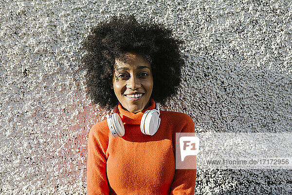 Happy young woman with headphones against wall in sunlight