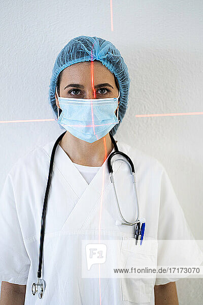 Junge Ärztin mit Laserlicht im Gesicht an der Wand einer Klinik