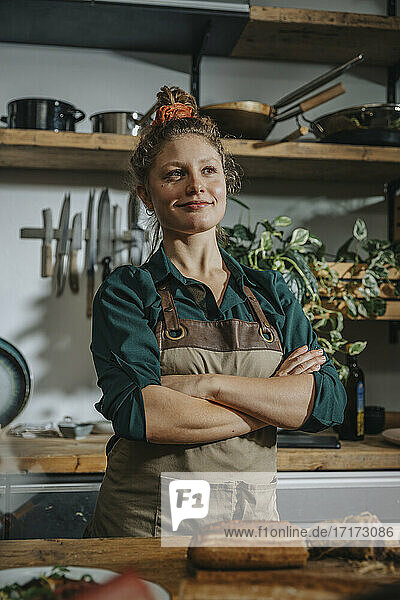 Confident female chef looking away while standing with arms crossed in kitchen