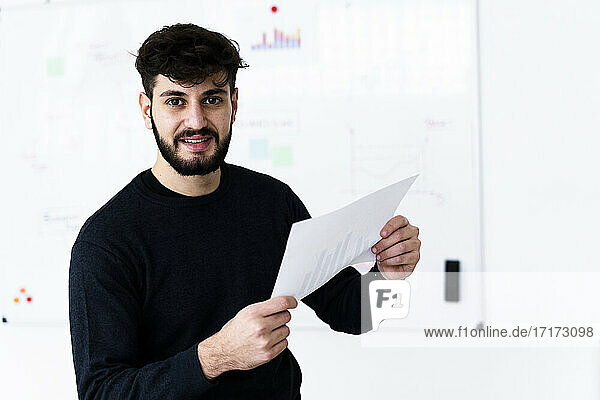Porträt eines jungen Geschäftsmannes  der ein Dokument im Konferenzraum eines Kreativbüros hält