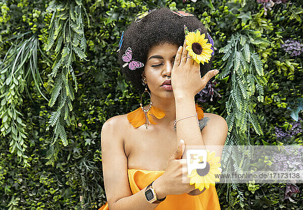 Young woman covering eye with hand against plant