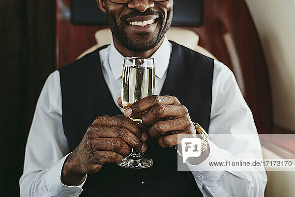 Smiling businessman holding champagne in private jet