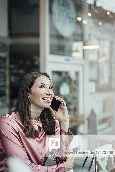 Lächelnde weibliche Fachkraft  die in einem Café mit einem Mobiltelefon spricht
