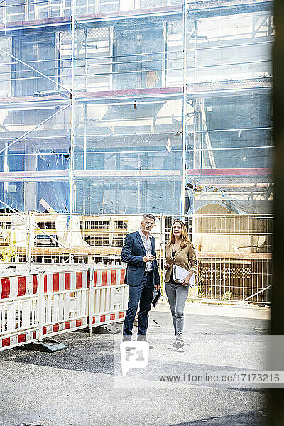 Bauunternehmer  der eine Baustelle mit einer Geschäftsfrau begutachtet  während er am Gebäude steht