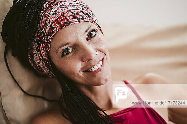 Lächelnde Frau mit Kopftuch  die sich zu Hause auf dem Sofa ausruht