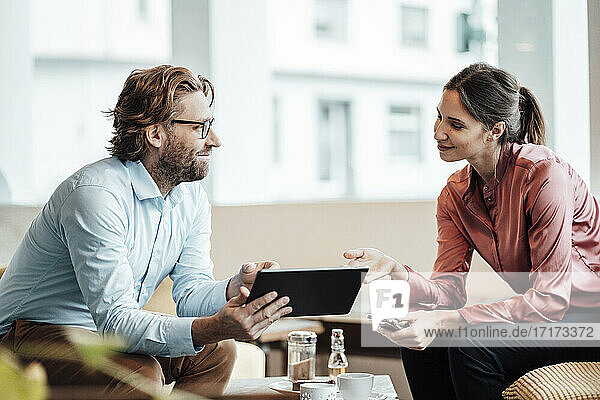 Lächelnde männliche und weibliche Kollegen  die über ein digitales Tablet während eines Treffens in einem Café diskutieren