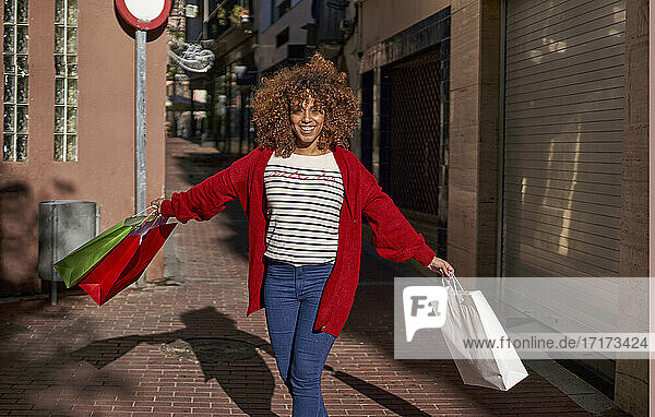 Carefree woman holding shopping bags while running on footpath