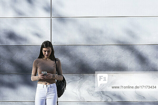 Female entrepreneur using mobile phone while standing against wall