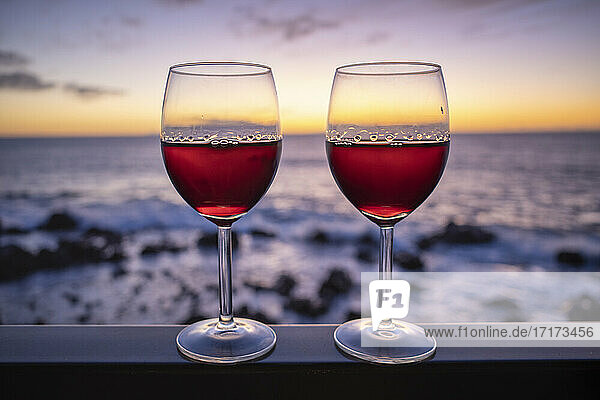 Zwei Gläser Rotwein mit Meer bei Sonnenuntergang im Hintergrund