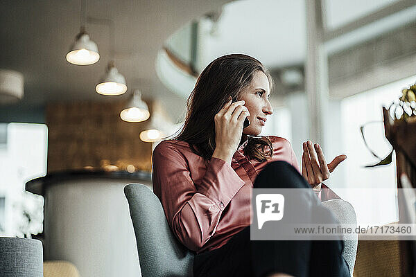 Female professional gesturing while talking on phone call in cafe