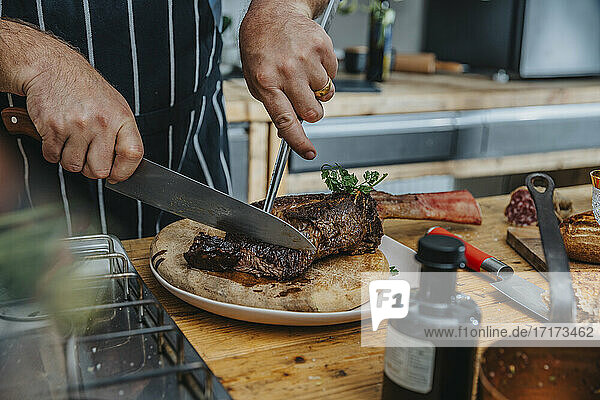 Expertise cutting cooked tomahawk steak in plate while standing in kitchen