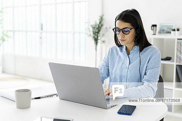 Female customer service representative with headset working on laptop while sitting at office