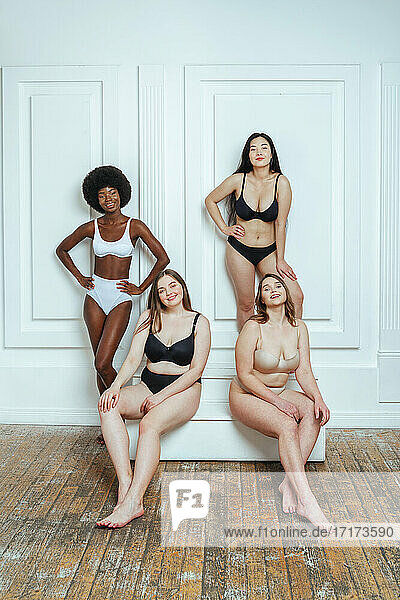 Multi-ethnische Gruppe von Model-Freundinnen in Dessous lächelnd gegen weiße Wand