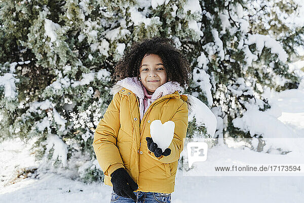Smiling cute girl holding heart shaped snow in park