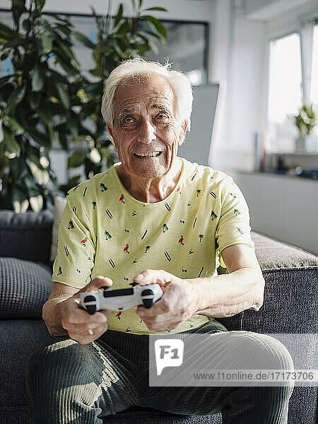 Älterer Geschäftsmann spielt ein Handheld-Videospiel  während er auf dem Sofa im Büro sitzt