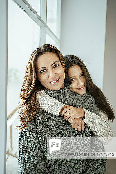 Lächelndes Mädchen  das seine Mutter umarmt  während es zu Hause sitzt