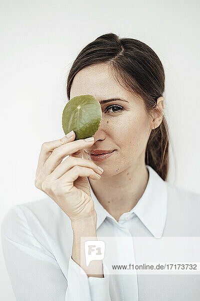 Elegant businesswoman holding leaf on her eye against white background in studio