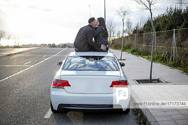 Junges Paar küsst sich auf dem Autodach sitzend