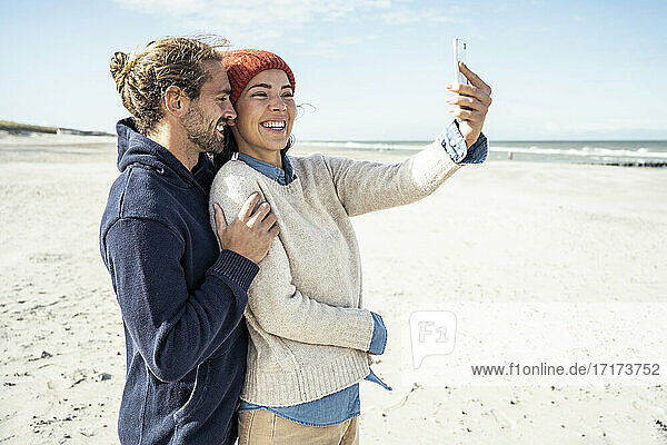 Portrait of young couple standing together on beach and using smart phone