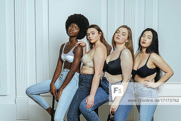 Multi-ethnic group of women wearing bras and jeans against wall