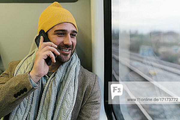 Smiling man wearing knit hat talking on mobile phone while sitting in train