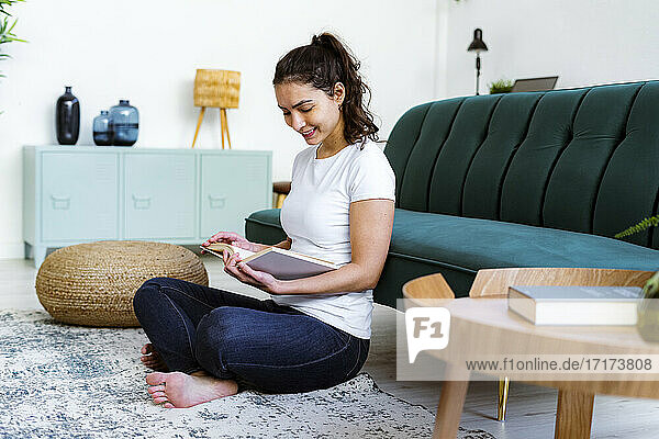 Woman smiling while reading book sitting at home