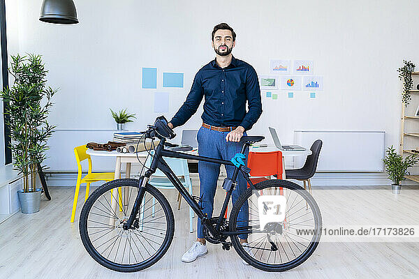 Male entrepreneur standing with bicycle in office