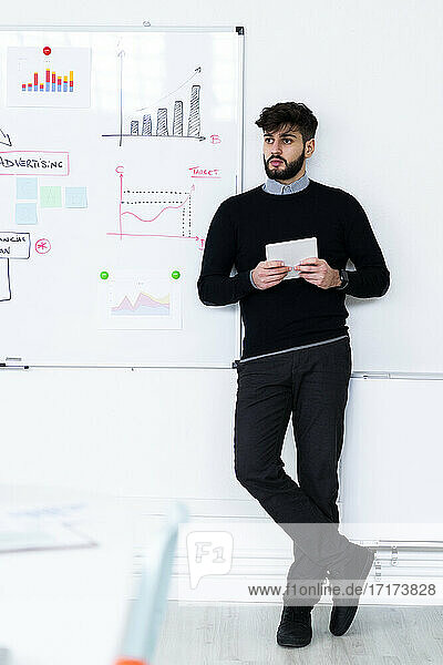 Businessman with digital tablet standing in front of whiteboard in office