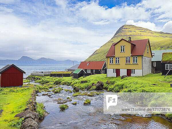 Stream flowing by houses against cloudy sky  Iceland