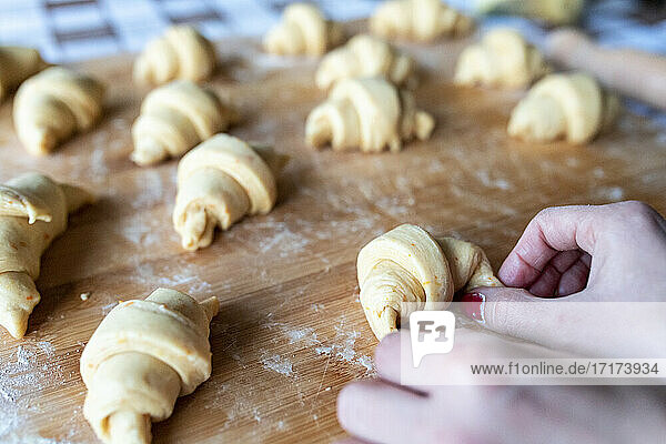 Woman shaping croissants on wooden cutting board in kitchen
