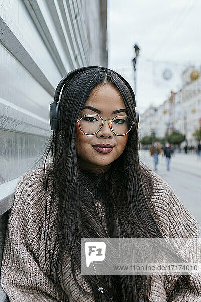 Beautiful woman with headphones against metal wall in city