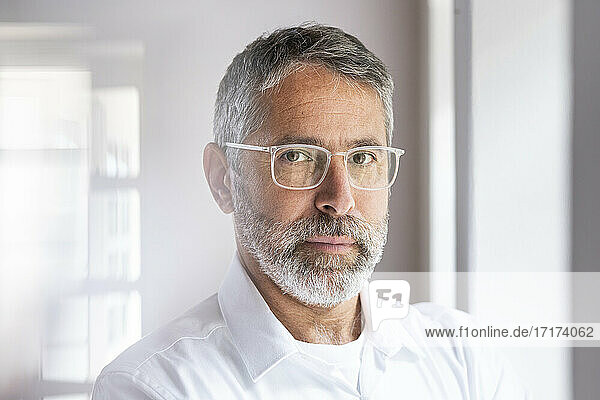 Confident businessman wearing eyeglasses staring while standing at home