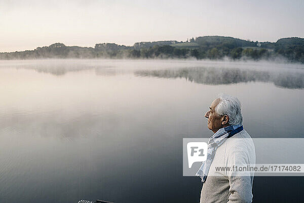 Senior man looking at view while standing against lake