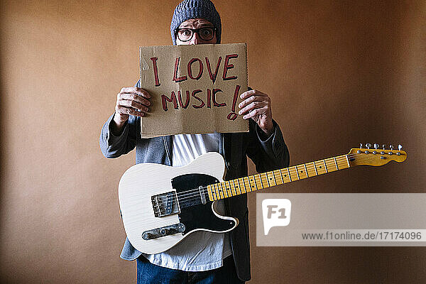 Male musician holding paper with text against brown wall