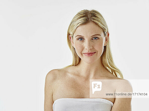 Woman wrapped in towel smiling while standing against white background