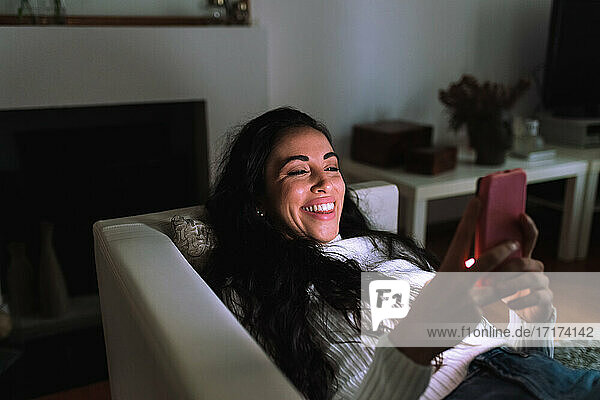 Young woman on sofa  smiling at mobile phone