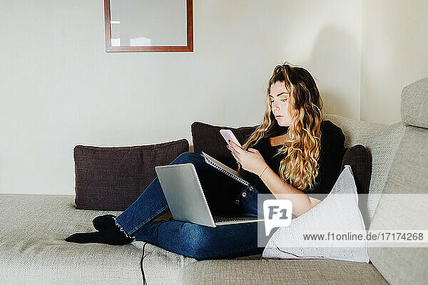 Junge Frau nutzt Smartphone und Laptop zu Hause