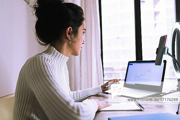 Young woman working from home with laptop  phone and ring light