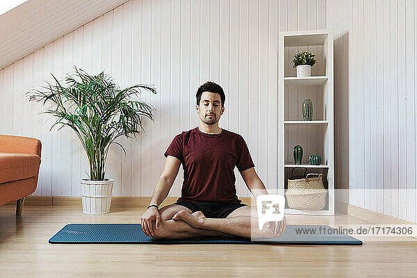 Mann meditiert zu Hause  sitzend mit gekreuzten Beinen