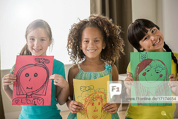 Drei Mädchen halten Zeichnungen von Gesichtern