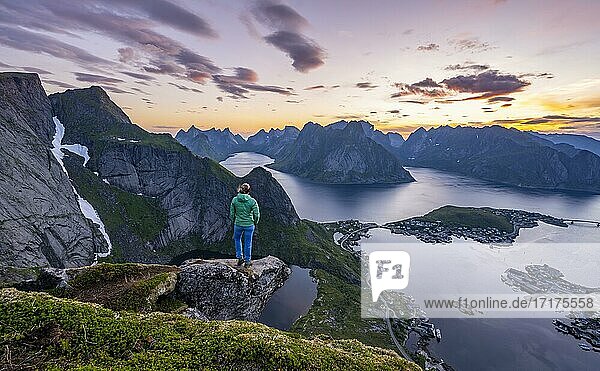 Evening atmosphere  young hiker standing on a rocky outcrop and enjoying the view from Reinebringen  Reinebriggen  Hamnoy  Reine and the Reinefjord with mountains  Moskenes  Moskenesöy  Lofoten  Norway  Europe