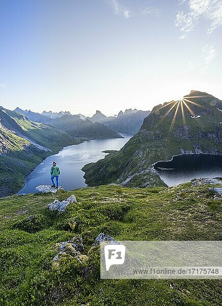 Junge Frau blickt über Fjordlandschaft  Sonne strahlt über Berglandschaft mit Fjord Forsfjorden und See Krokvatnet  Moskenesöy  Lofoten  Nordland  Norwegen  Europa