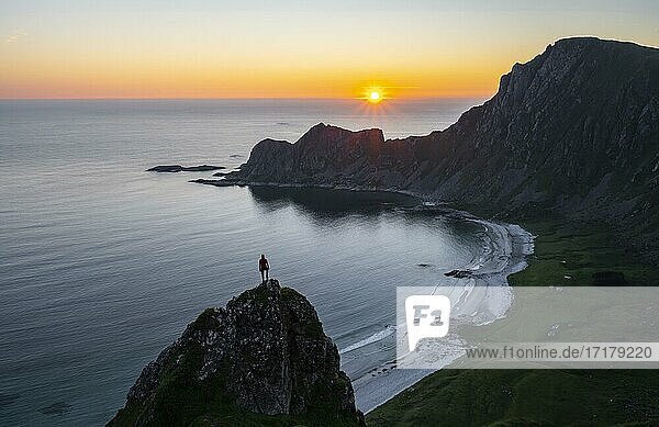Sunset  hiker on rocks  cliffs  beach and sea  behind summit of mountain Måtinden  near Stave  Nordland  Norway  Europe