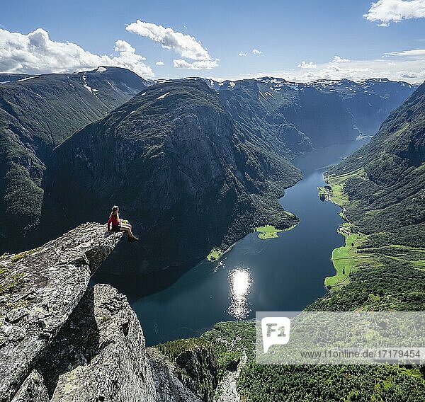 Hiker sitting on rock  view from the top of Breiskrednosi  mountains and fjord  Nærøyfjord  Aurland  Norway  Europe
