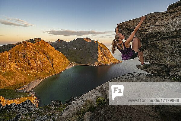 Abendstimmung  Junge Frau beim Bouldern  klettern  Gipfel des Ryten  Meer  Kvalvika Strand und Berge  Fredvang  Lofoten  Nordland  Norwegen  Europa